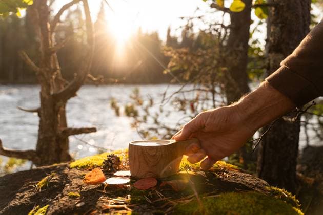 A cropped unrecognizable man enjoys a warm coffee by a serene lake in the golden light of a Swedish autumn afternoon. Model Released AlbaVitta_ID24460_709006_007 Copyright: xAlbaxVittax RECORD DATE NOT STATED