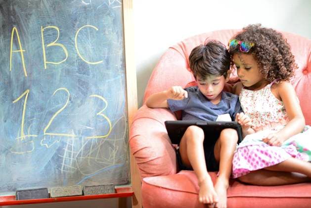Two children sharing a tablet while sitting on a pink chair next United States, Florida, Inverness CR_YWQX241014-1556235-01 ,model released, Symbolfoto