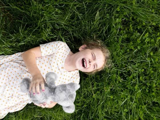 Creative Highlights Symbolfotos A girl lies in the grass, laughing and holding a stuffed animal Corvallis, Montana, United States CR_STTH241022-1566600-01 ,model released, Symbolfoto