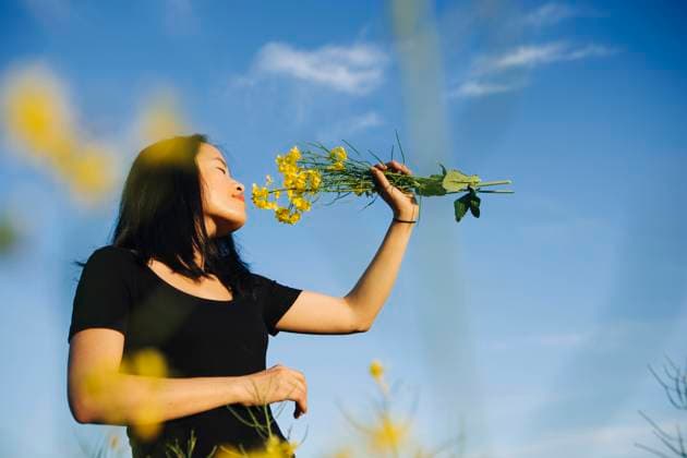IMAGO Creative, Frühling, Licht und Sonne Young woman smelling yellow flowers under blue sky model released, Symbolfoto, OJF00534
