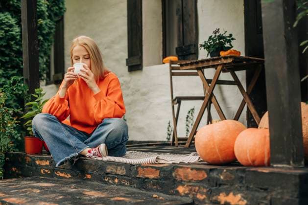 Woman drinking coffee sitting cross-legged on porch in autumn model released, Symbolfoto property released, VSNF02494