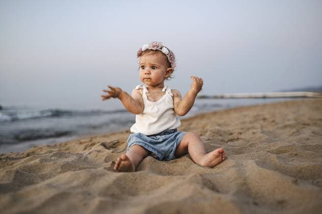 Ein nachdenklich Baby in sommerlicher Kleidung und Blumenschmuck im Haar sitzt am Strand bei Sonnenuntergang A thoughtful baby in summery clothes and flowers in her hair sits on the beach at sunset Copyright: imageBROKER ThomasxBaur ibxtba11635033.jpg ,model released, Symbolfoto ,property released