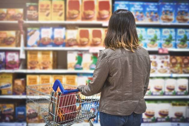 Customer, woman and shopping at grocery store in shelf with wheel cart, food and product. Female person, back and supermarket or convenience shop for retail cost, prices and discounts or promotion. model released property released Copyright: xwww.peopleimages.comx