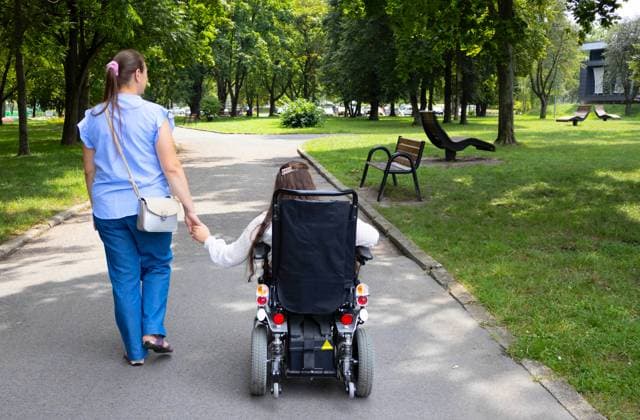 A young girl in a motorized wheelchair is accompanied by family member on a leisurely walk through a park The image captures a moment of inclusion and mobility assistance during a family outing Model Released HalynaDorozhynska_ID24076_697452_007 Copyright: xHalynaxDorozhynskax RECORD DATE NOT STATED