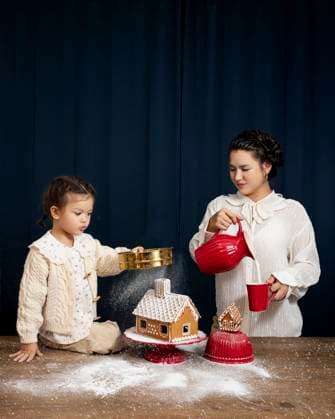 Creative Highlights Symbolfotos A mother and her young child enjoy a festive moment, decorating a detailed gingerbread house together The dark backdrop contrasts with their bright holiday attire and the sprinkle of snow-like sugar Model Released KateSurzhok_ID24536_711320_003 Copyright: xKatexSurzhokx RECORD DATE NOT STATED