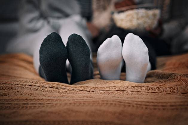 Feet, socks and people relax on bed at house for watching tv, movie night and bonding with popcorn in winter. Friends, legs and bedroom for streaming show, media and snacks of entertainment at home. model released property released Copyright: xwww.peopleimages.comx