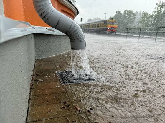 Gutter by the wall of the building and train in the background, rapid flow of water after heavy rain. Copyright: xx