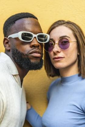 Vertikale Nahaufnahme eines stilvollen multirassischen Paares mit Sonnenbrille, das gemeinsam in die Kamera schaut, vor einem gelben Hintergrund Vertical close-up photo of a stylish multiracial couple wearing sunglasses looking at camera together against yellow background Copyright: imageBROKER UnaixHuizi ibxuhu11646121.jpg ,model released, Symbolfoto ,property released