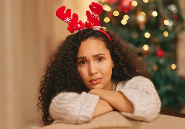 Portrait, lonely and sad woman on couch at Christmas with crisis, frustrated face and holiday in lounge at home. Mental health, vacation and girl with depression on sofa in living room with xmas tree. model released property released Copyright: xYURIxARCURSxPRODUCTIONSx