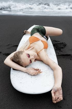 Weibliche Surferin genießt wohlverdiente Pause auf schwarzem Sandstrand, liegend auf weißem Surfbrett mit geschlossenen Augen. Sinnlichkeit Sport Mode Modell sieht so entspannt nach einem intensiven Sport Training Sitzung Female surfer is enjoying well deserved break on black sandy beach, lying on white surfboard with eyes closed. Sensuality sports fashion model looks so relaxed after an intense sports training session Copyright: imageBROKER AlexanderxA.xPiragis ibxiqx11670559.jpg ,model released, Symbolfoto ,property released