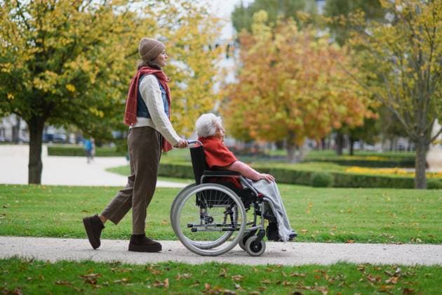 Granddaughter on an autumn walk in the park with her grandmother, pushing her in wheelchair. Side view. Granddaughter on an autumn walk in the park with her grandmother, pushing her in wheelchair. model released