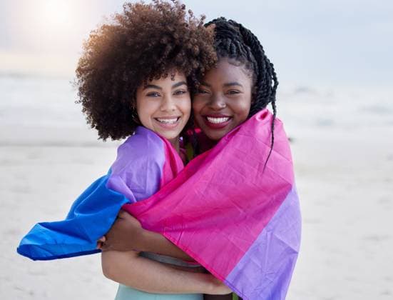 IMAGO Creative, Diversity, Teenager: LGBTQIA+ Love, beach and portrait of lesbian couple with flag, hug and happy holiday together in Pride Month. Smile, embrace and lgbt women relax on ocean vacation for romantic date, support and trans culture. model released property released Copyright: xwww.peopleimages.comx