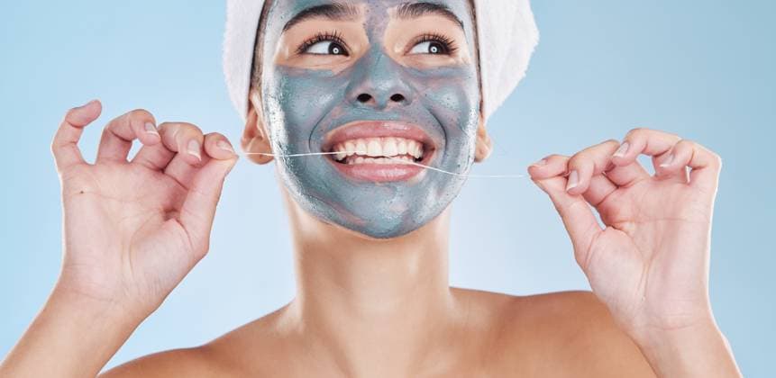 Creative Highlights Symbolfotos Dental, face mask and woman flossing teeth in a skincare beauty studio portrait with a blue background. Wellness, smile and happy girl grooming and cleaning her mouth and facial pores to be healthy. model released property released Copyright: xwww.peopleimages.comx