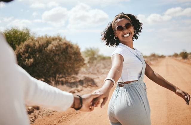 Creative Highlights Symbolfotos Couple, walking and nature with a black woman and man outdoor holding hands on a sand road in a dessert together. Travel, love and romance with a female and male on a date during summer vacation. model released property released Copyright: xwww.peopleimages.comx