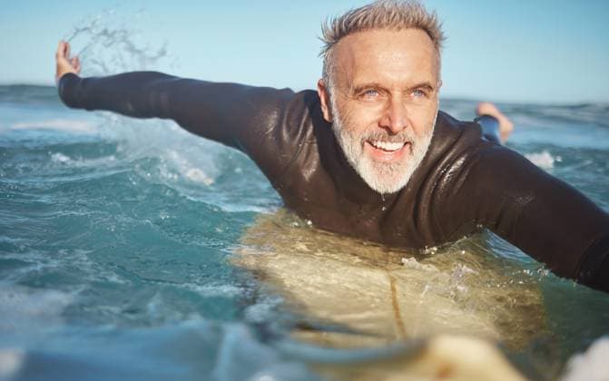 Creative Highlights Symbolfotos Beach, water and old man surfer swimming on a summer holiday vacation in retirement with freedom in Bali. Smile, ocean and senior surfing or body boarding enjoying a healthy exercise on sea of Island. model released property released Copyright: xwww.peopleimages.comx