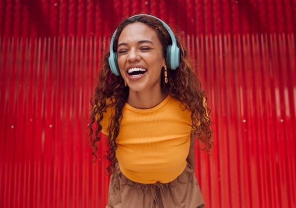 Creative Highlights Symbolfotos Urban, joy and woman with headphone music enjoying happy rhythm with bluetooth connection. Smile of latino girl listening to feel good streaming audio while resting at wall for leisure break model released property released Copyright: xwww.peopleimages.comx