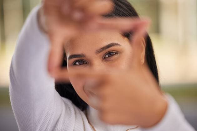 Creative Highlights Symbolfotos Hands, frame and eyes with a woman looking through her fingers while framing her face outdoor. Portrait, girl and happy with a young female posing behind a hand sign on a blurry background outside. model released property released Copyright: xwww.peopleimages.comx