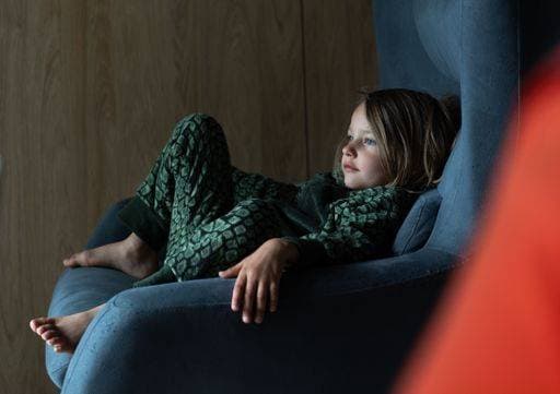 Creative Highlights Symbolbilder Young girl in green and white pajamas reclines in a blue armchair, gazing thoughtfully to the side with a wooden wall in the background. 25821771 ,model released, Symbolfoto RECORD DATE NOT STATED