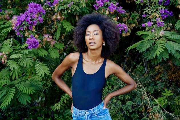 Creative Highlights Symbolbilder Napoli blooms Confident woman with afro hair standing against a backdrop of vibrant purple flowers and lush green foliage. Naples Italy bola03896 Copyright: xConnectxImagesx ,model released
