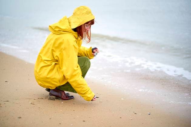 Person in a yellow raincoat crouching on a sandy beach collecting shells, Belgium bola04947 Copyright: xConnectxImagesx ,model released