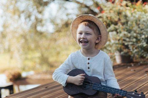 Creative Highlights Symbolbilder Young boy with straw hat playing ukulele outdoors, smiling joyfully on a sunny day. 26996604 ,model released, Symbolfoto RECORD DATE NOT STATED