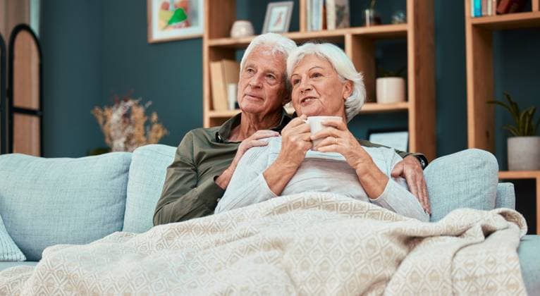 Relax, love and coffee with old couple on sofa with blanket for cuddling, affectionate or watching tv. Cozy, comfortable and retirement with man and woman in living room for break, marriage or lounge. model released property released Copyright: xwww.peopleimages.comx