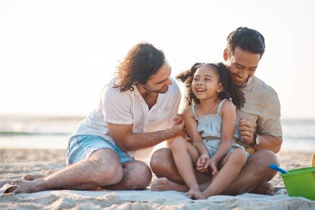 Gay men, dad and girl at beach with love, bonding and care for vacation, laughing and outdoor in sunshine. LGBTQ couple, young child and adoption with family, holiday and comic conversation in summer. model released property released Copyright: xwww.peopleimages.comx