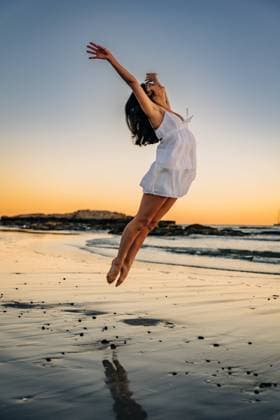Creative Highlights Symbolbilder Woman joyfully leaping on beach at sunset with arms extended Gloucester, Massachusetts, United States CR_FKNH241030-1571754-01 ,model released, Symbolfoto