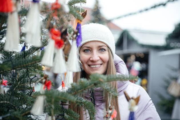 IMAGO Creative, Winter, In der Stadt Smiling woman in white hat near Christmas tree Klagenfurt am Wörthersee, Carinthia, Austria R_GVYI241030-1573408-01 ,model released, Symbolfoto