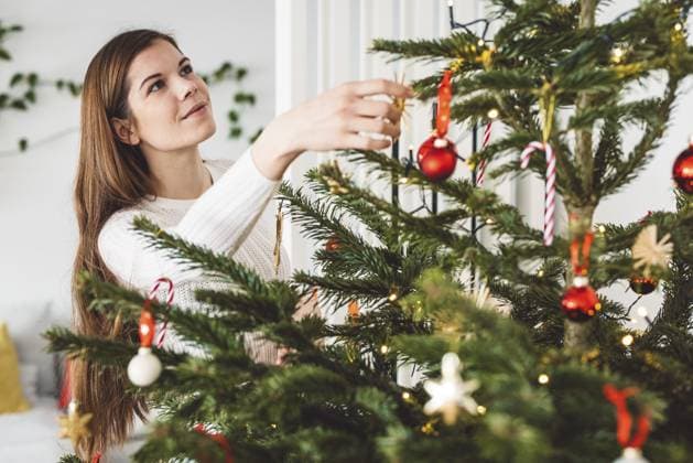 Schöne, lächelnde, fröhliche, kaukasische Frau in weißem Outfit schmückt einen natürlichen Weihnachtsbaum, steckt rote Ornamente auf den Baum, hält ein rotes Weihnachtsornament Beautiful smiling cheerful caucasian woman dressed in white outfit decorating a natural Christmas tree, putting red ornaments on the tree, holding a red Christmas ornament Copyright: imageBROKER ZigaxPlahutar ibxiqx11269236.jpg ,model released, Symbolfoto ,property released