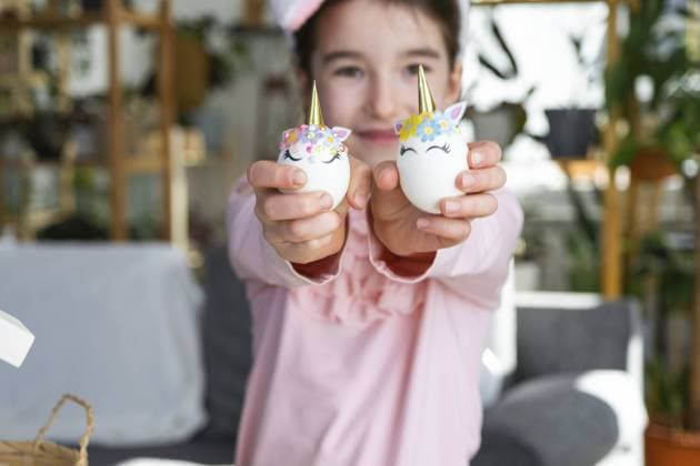 Ein niedliches Mädchen mit rosa Hasenohren macht ein Osterbasteln, dekoriert ein Ei in Form eines Einhorns mit Strasssteinen, Horn, Blumen im Inneren eines Hauses mit Pflanzen A cute girl with pink bunny ears makes an Easter craft, decorates an egg in the form of a unicorn with rhinestones, horn, flowers in the interior of a house with plants Copyright: imageBROKER OlgaxSimonova ibxiqx11185663.jpg ,model released, Symbolfoto ,property released