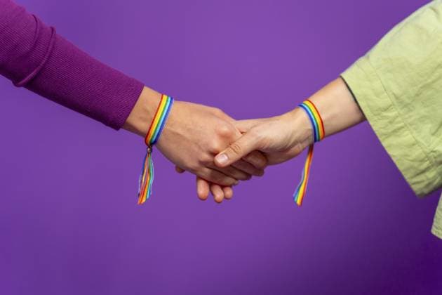 Studiofoto mit lila Hintergrund und Nahaufnahme von zwei lesbischen Frauen, die sich an den Händen halten und ein lgbt Regenbogenarmband tragen Studio photo with purple background and close-up of two lesbian woman holding hands wearing lgbt rainbow bracelet Copyright: imageBROKER UnaixHuizi ibxuhu11764014.jpg ,model released, Symbolfoto ,property released