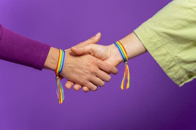Studiofoto mit lila Hintergrund von zwei nicht erkennbaren jungen lesbischen Paaren, die sich an den Händen halten und Regenbogenarmbänder tragen Studio photo with purple background of two unrecognizable Young lesbian couple holding hands, wearing rainbow bracelets Copyright: imageBROKER UnaixHuizi ibxuhu11764016.jpg ,model released, Symbolfoto ,property released