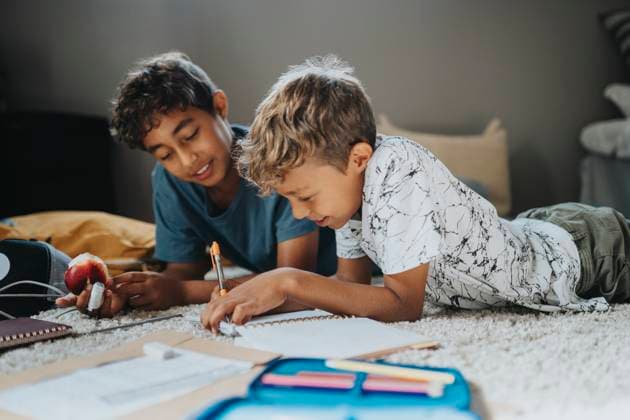 Multiracial boys doing homework while lying on front at home Sweden, Stockholm, model released, property released Copyright: xMaskotx , MA113029 MA113029