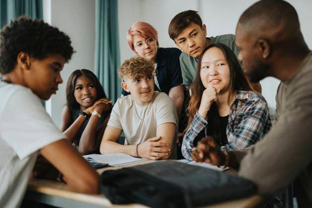 Teenage girls and boys with non-binary person looking at teacher discussing in classroom Sweden, Gothenburg, model released, property released Copyright: xMaskotx , MA113322 MA113322