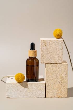 A sophisticated presentation of a dropper bottle on natural stone podiums adorned with bright yellow craspedia flowers, depicting a modern, eco-friendly cosmetics display. Model Released Ikvyatkovskaya_ID25032_725381_009 Copyright: xIkvyatkovskayax