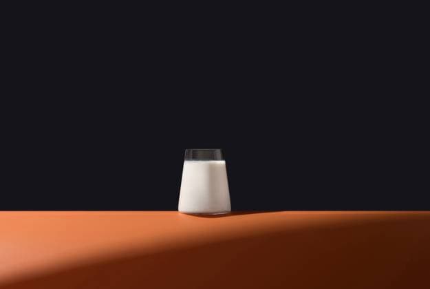 A simple and elegant image featuring a full glass of milk on a vibrant orange surface, set against a dark, contrasting background Ideal for showcasing purity and freshness Model Released RuthCarrodeguas_ID24758_717745_001 Copyright: xRuthxCarrodeguasx RECORD DATE NOT STATED
