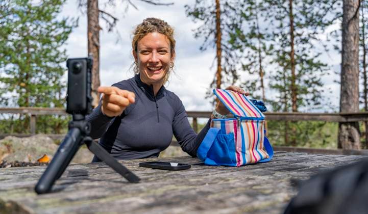 A joyful woman relishes her lunch outdoors while trekking in the serene Muddus National Park, located in Lapland, Sweden She is capturing the moment using a camera on a tripod Model Released VictorCuenca_ID24674_714855_004 Copyright: xVictorxCuencax