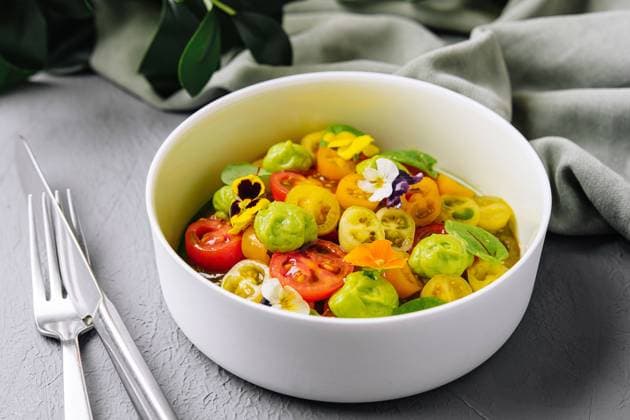 Frischer Tomatensalat mit essbaren Blüten Vibrant salad of cherry tomatoes and gooseberries garnished with edible flowers, served in a white bowl Copyright: xZoonar.com AntonxDobreax 22298559