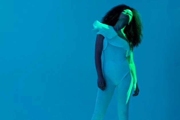 Creative Highlights Symbolbilder Eine Afrikanerin in weißem Gewand steht mit erhobener Hand auf türkisfarbenem Hintergrund An African in a white outfit stands with her hand raised on a turquoise background. An elegant black girl is illuminated by green neon lights. A woman in an elegant bodysuit poses in the spotlight ,model released, Symbolfoto Copyright: xZoonar.com DashaxPetrenkox 22303750 ,model released, Symbolfoto ,property released
