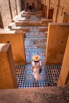 Creative Highlights Symbolbilder Woman in white dress and hat walking through historic Moroccan palace with intricate tile patterns and warm tones. 27468777 ,model released, Symbolfoto RECORD DATE NOT STATED