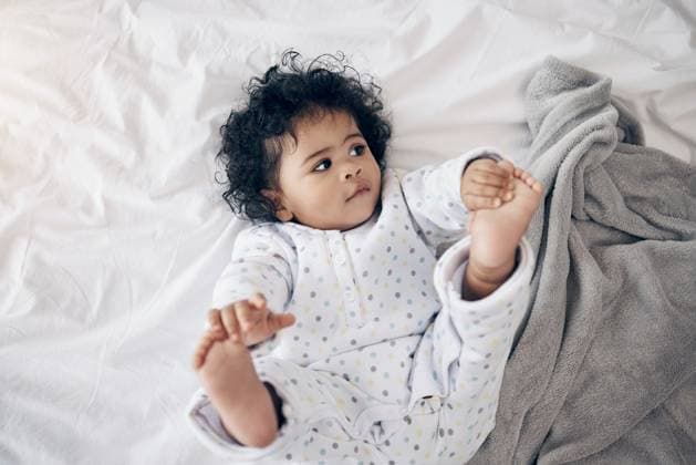 Creative Highlights Symbolbilder Baby, relax and playing with toes in home, nursery bed and dream of care in bedroom for development. Child, learning motor skills and curious on growth on blanket, infant and morning for stretching. model released property released Copyright: xwww,peopleimages.comx