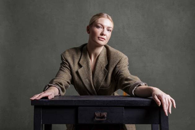 Creative Highlights Symbolbilder 783449156 Frau sitzt ernst an einem dunklen Tisch vor grünem Hintergrund in schicker Kleidung, Fotoshooting Woman sitting seriously at a dark table in front of a green background in smart clothes, photo shoot Copyright: imageBROKER RonaldxMitterer ibxrmr11829814.jpg ,model released, Symbolfoto ,property released