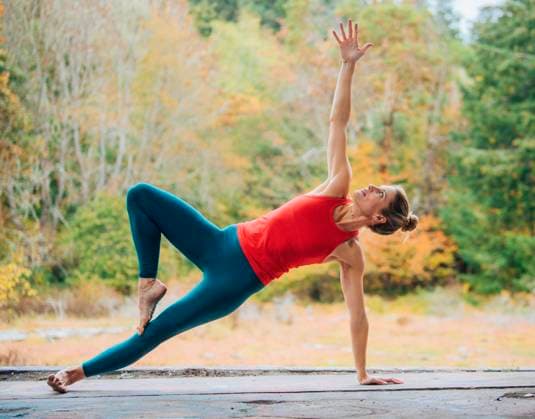 Woman performs a side plank yoga pose outdoors on a wooden deck with autumn trees in the background, USA sape00323 Copyright: xConnectxImagesx ,model released