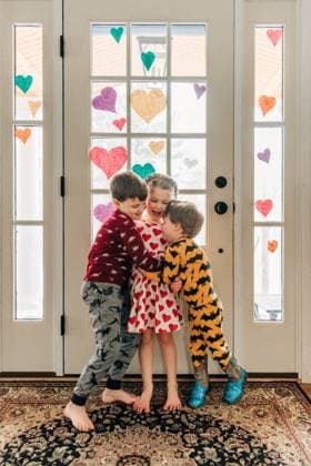 Three siblings hug and laugh together near heart-decorated doors North Andover, Massachusetts, United States CR_FKNH241202-1584318-01 ,model released, Symbolfoto