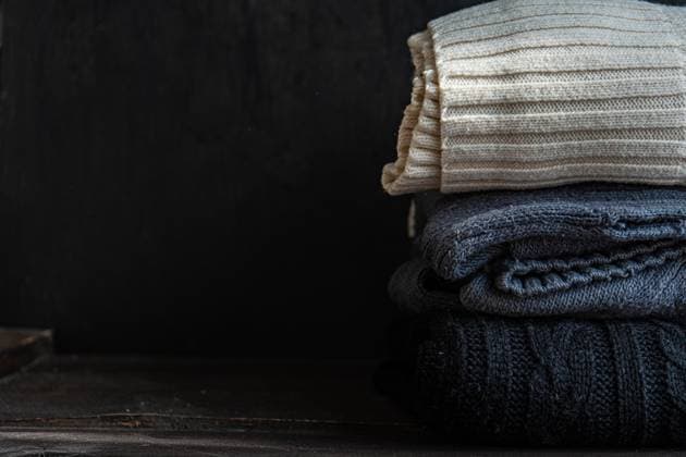 A neatly folded stack of cozy knitted sweaters in neutral tones lies on a rustic wooden surface, showcasing a warm and stylish fashion statement for chilly weather Model Released AnnaBogush_ID25071_726325_009 Copyright: xAnnaxBogushx RECORD DATE NOT STATED