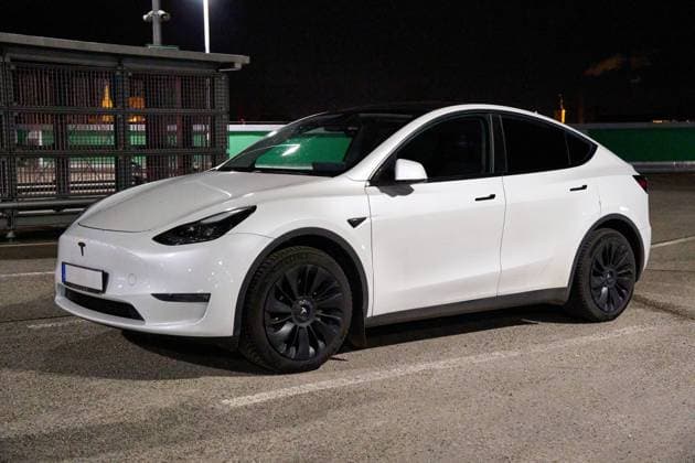 Ein weißes Elektroauto, Tesla Model Y, geparkt auf einem offenen Parkplatz bei Nacht im dunklen. Die Szene zeigt ein Auto im Alltagseinsatz mit Beleuchtung und Parkstruktur im Hintergrund.
