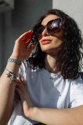 IMAGO Creative, Frühling, Licht und Sonne Sommer modische weibliche Porträt eines schönen lockigen Mädchen mit stilvollen Vintage-Sonnenbrille in einem weißen T-Shirt sitzt auf der Straße im Licht der Sonne *** Summer stylish Female Portrait one beautiful curl Girls with stylish Vintage Sunglasses in a white T Shirt sits at the Street at Light the Sun 1102819908 ,model released, Symbolfoto