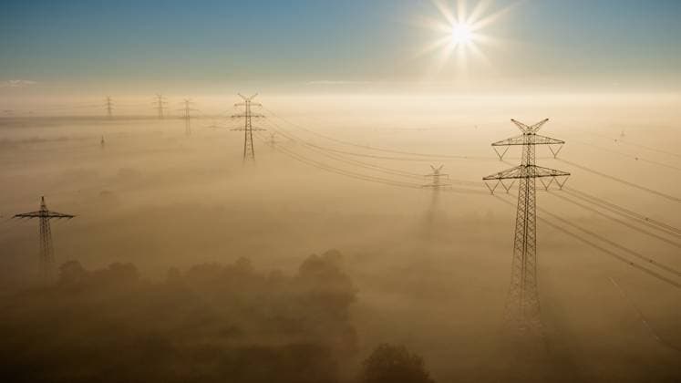 Blick auf Hochspannungsleitungen, die sich bei Sonnenaufgang durch eine nebelverhangene Landschaft ziehen, mit goldenen View of high-voltage power lines stretching through a mist-covered landscape at sunrise, with golden light casting long shadows and illuminating the fog-draped fields. Copyright: xZoonar.com FrederickxDörschemx 22327915