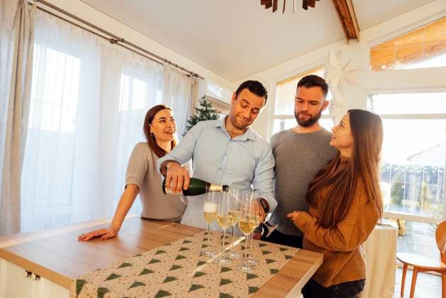 Ein lächelnder junger Mann schenkt im Esszimmer des Hauses Champagner in Gläser ein. Zwei attraktive Ehepaare feiern den Weihnachtsabend. Smiling young man pours champagne into glasses in dining room of house. Two attractive married couples are celebrating Christmas Eve. Happy friends celebrate new year together. House party. ,model released, Symbolfoto Copyright: xZoonar.com DashaxPetrenkox 22404552 ,model released, Symbolfoto ,property released
